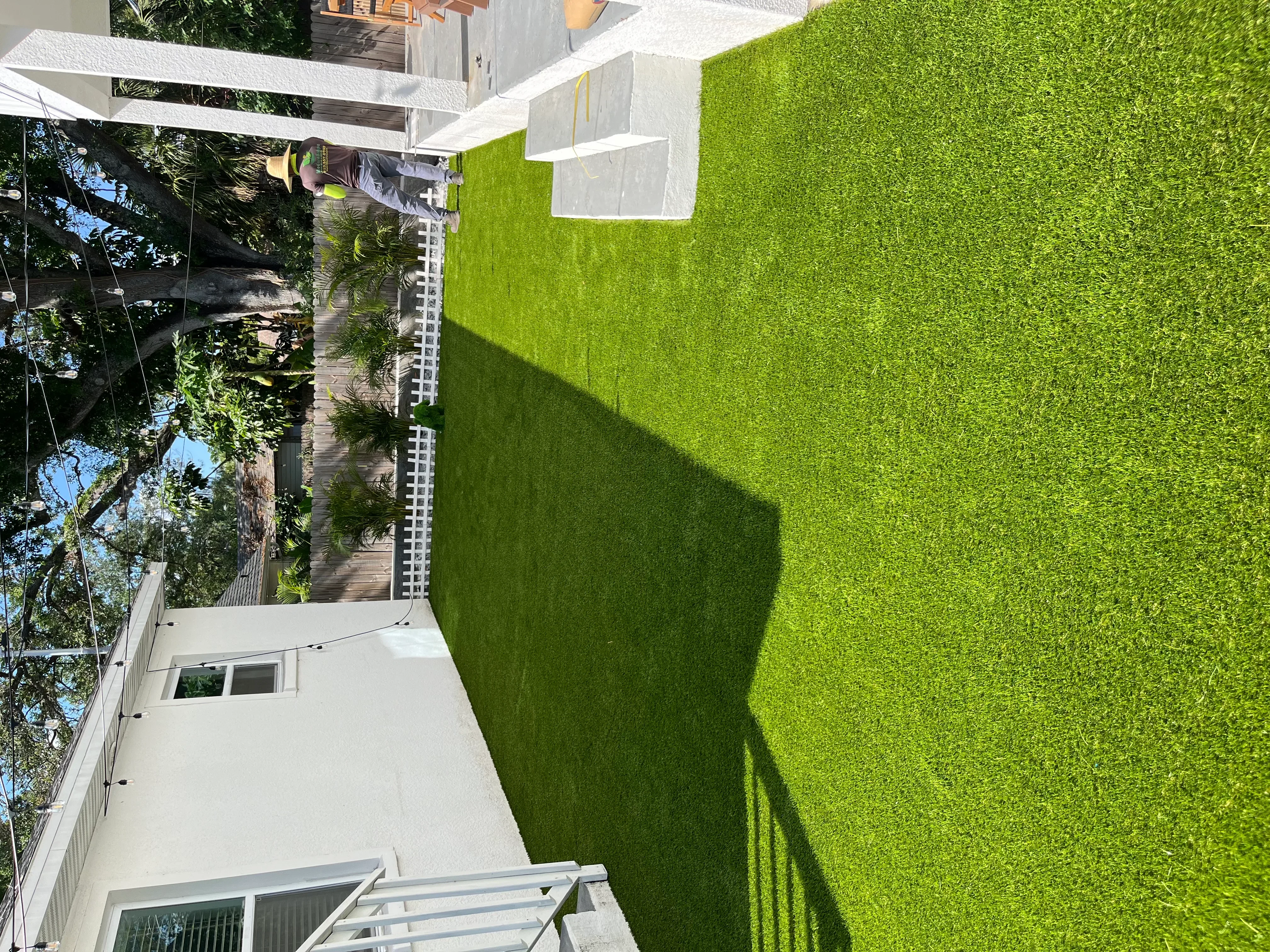 Bright green artificial turf lawn with white fence and pergola in modern residential backyard
