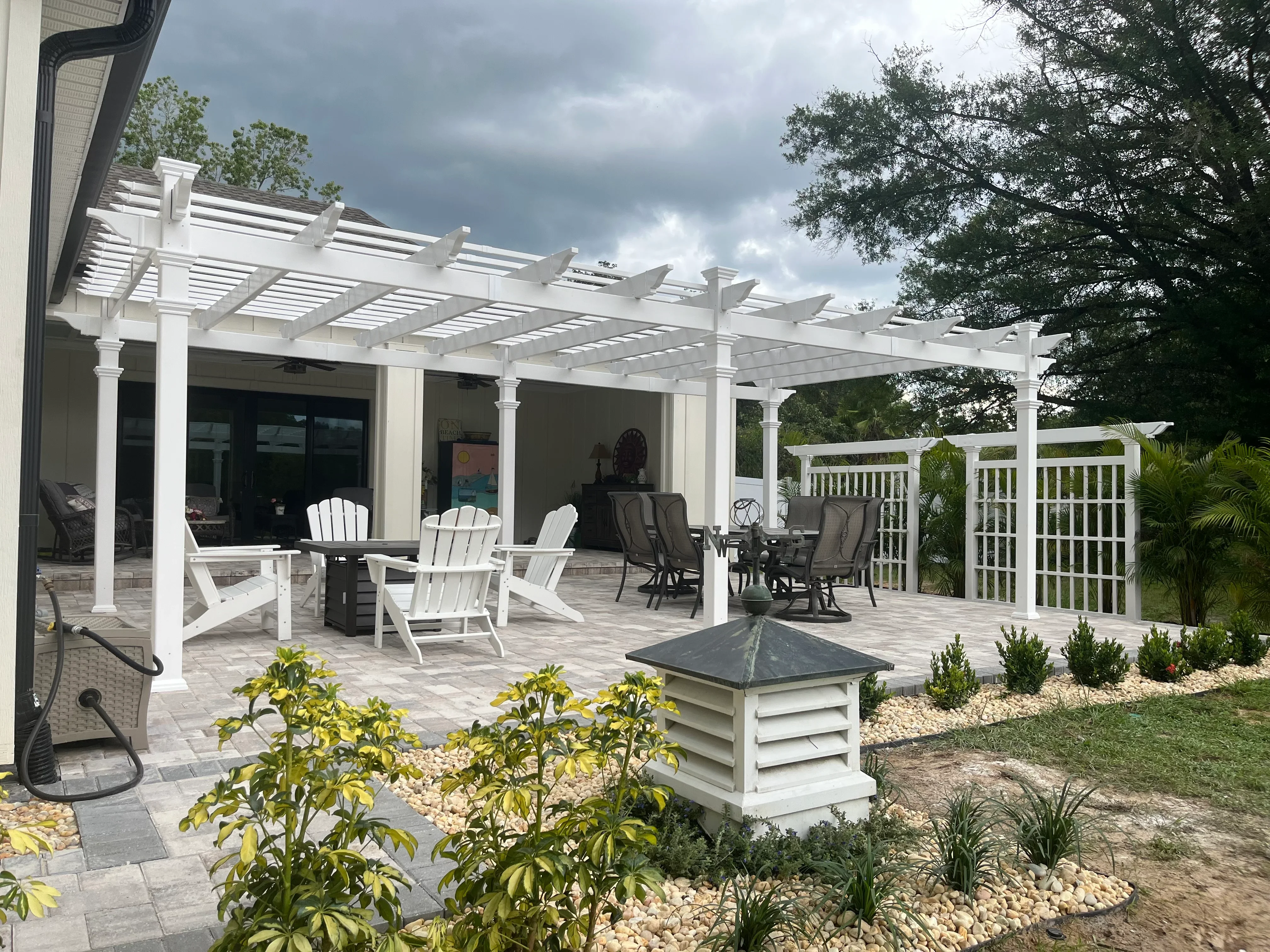 White vinyl pergola with louvered roof over paver patio, privacy screens, and landscaped beds with plantings
