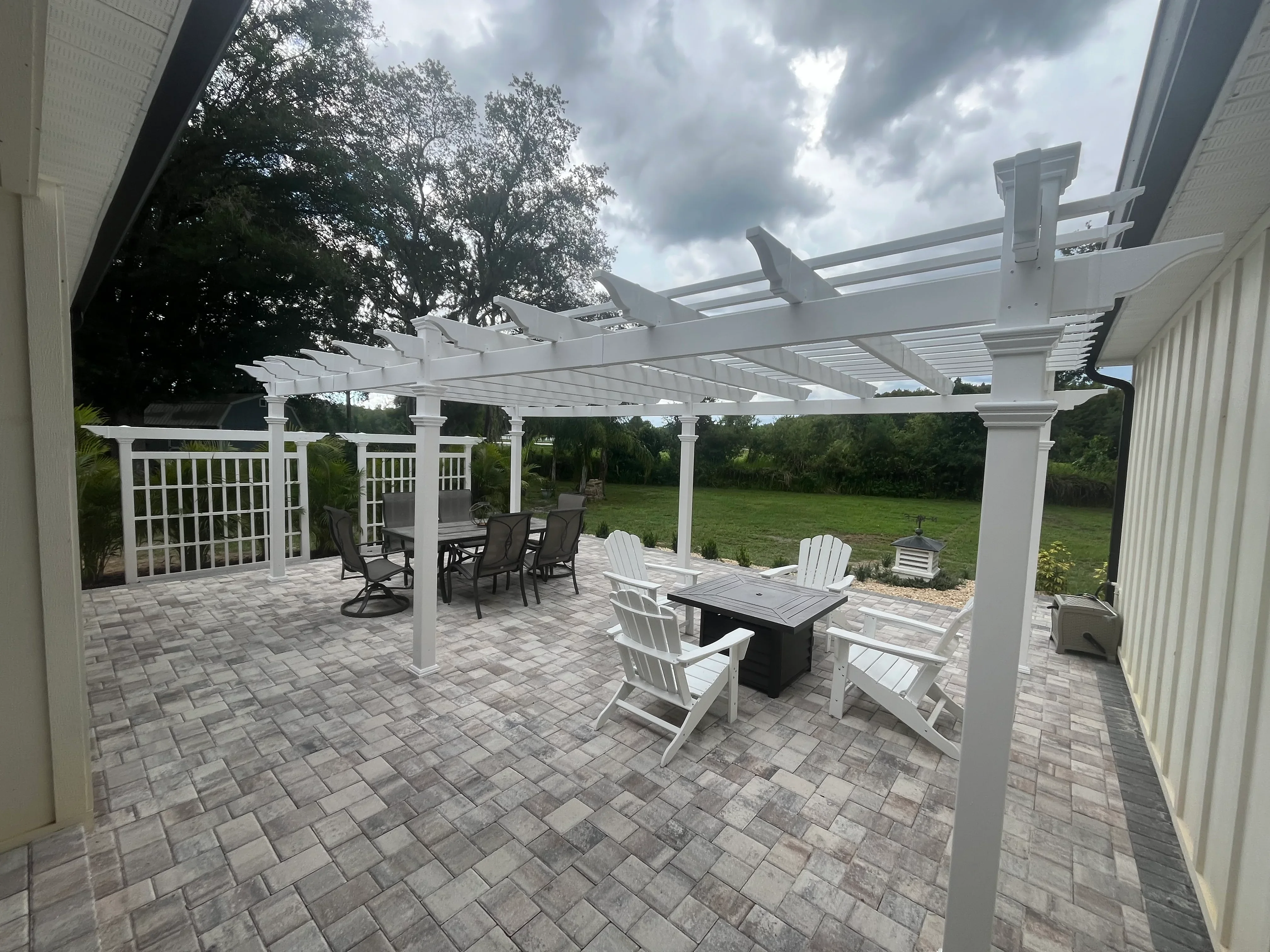 White vinyl pergola over paver patio with seating areas and fire table