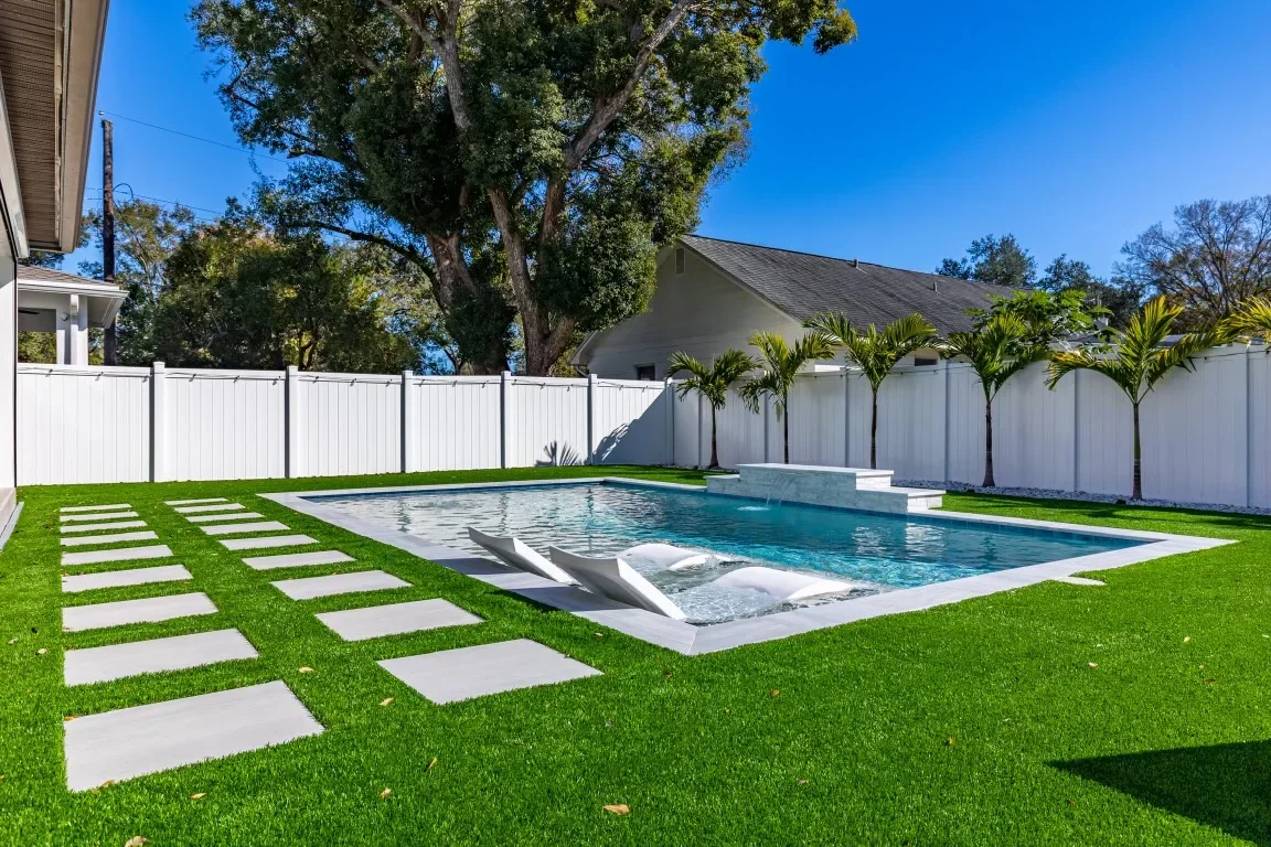 Pool landscape with concrete pavers, sod lawn, palm trees, and white vinyl fence