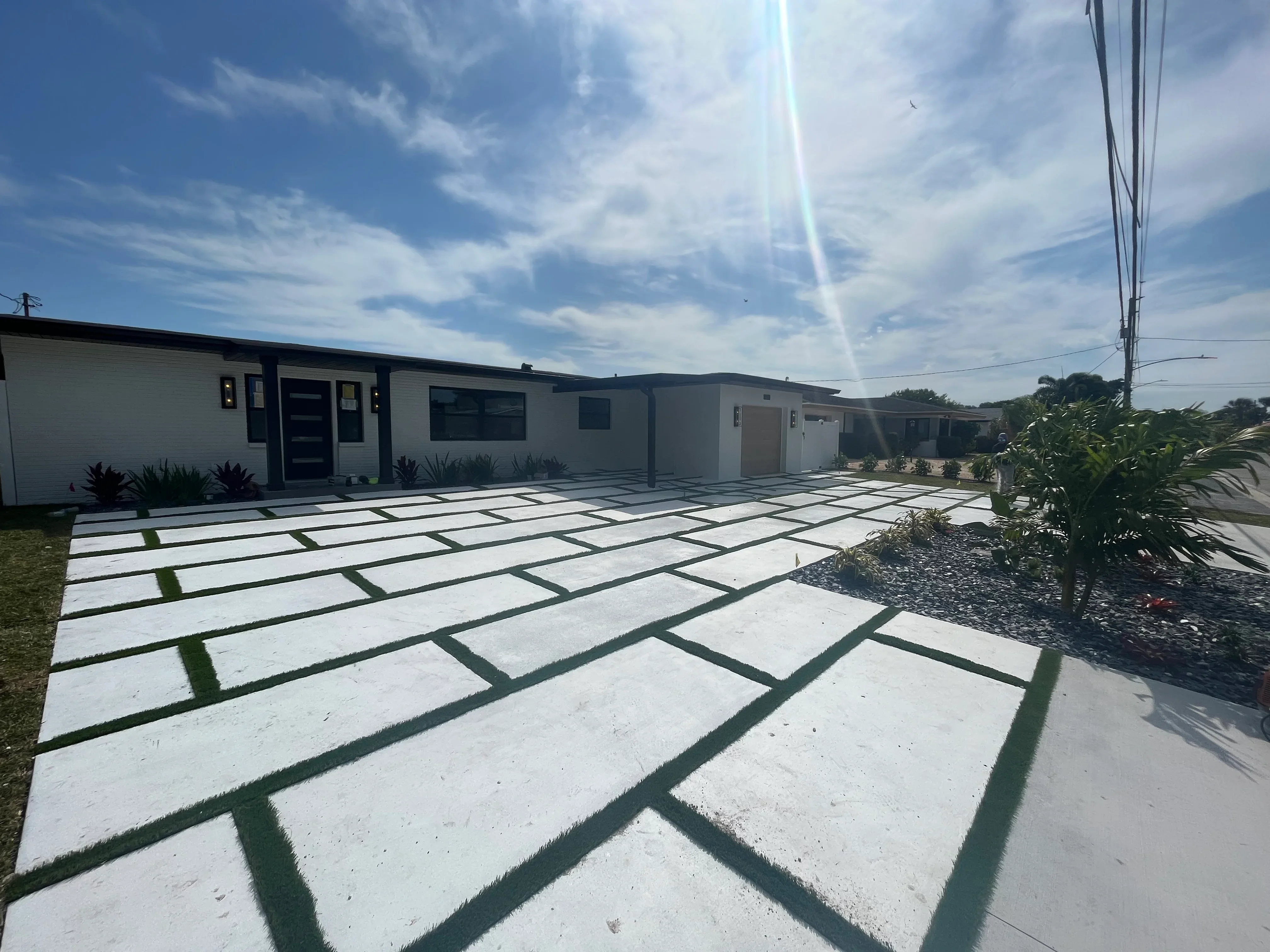 Geometric concrete pavers with grass strips in front of modern white home with black trim