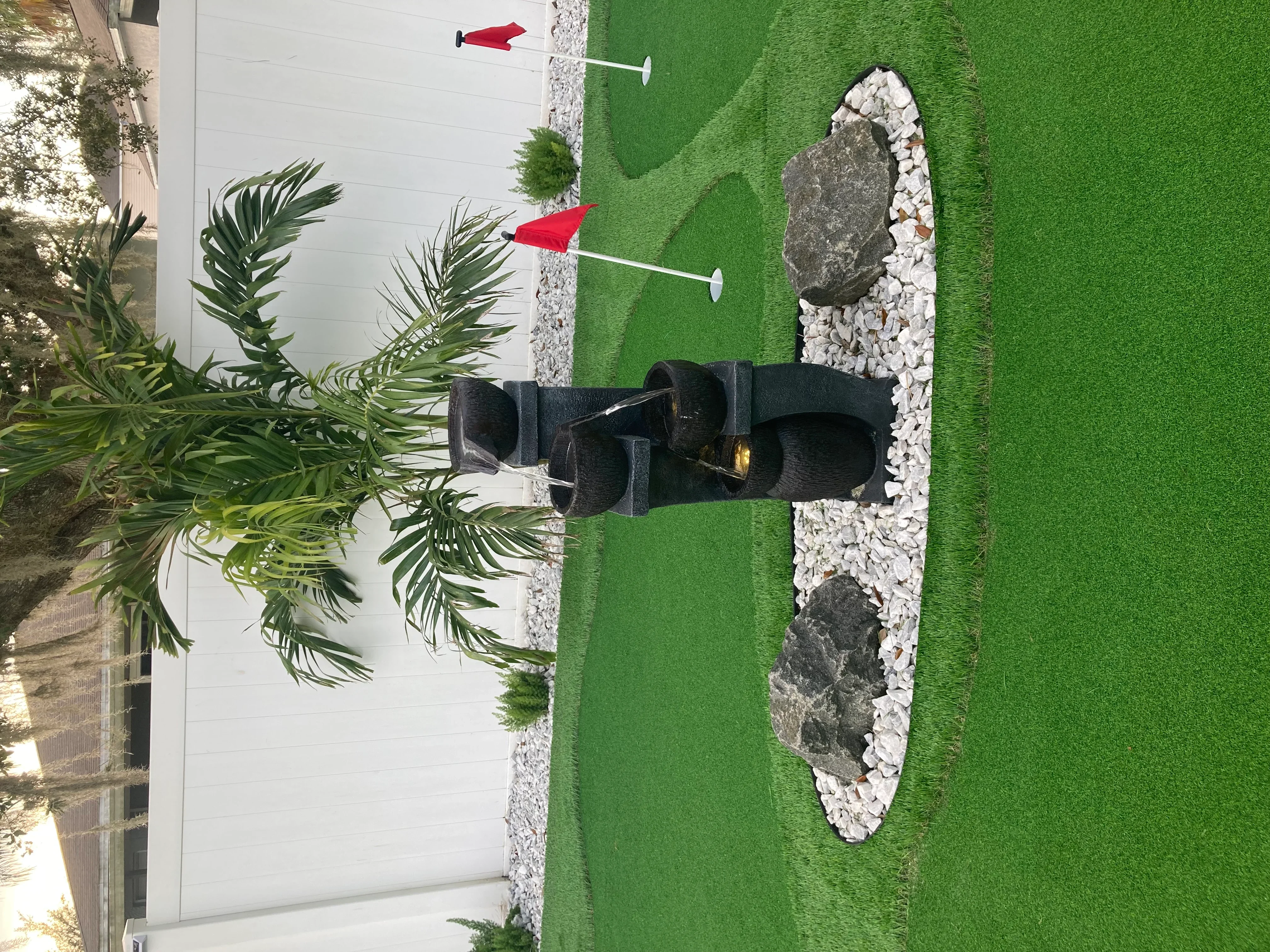 Synthetic turf with white pea gravel border, natural stone boulders, and black planter feature