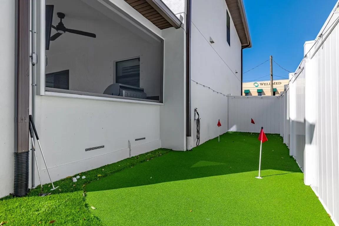 Synthetic putting green with multiple holes, white vinyl fence, and modern patio structure