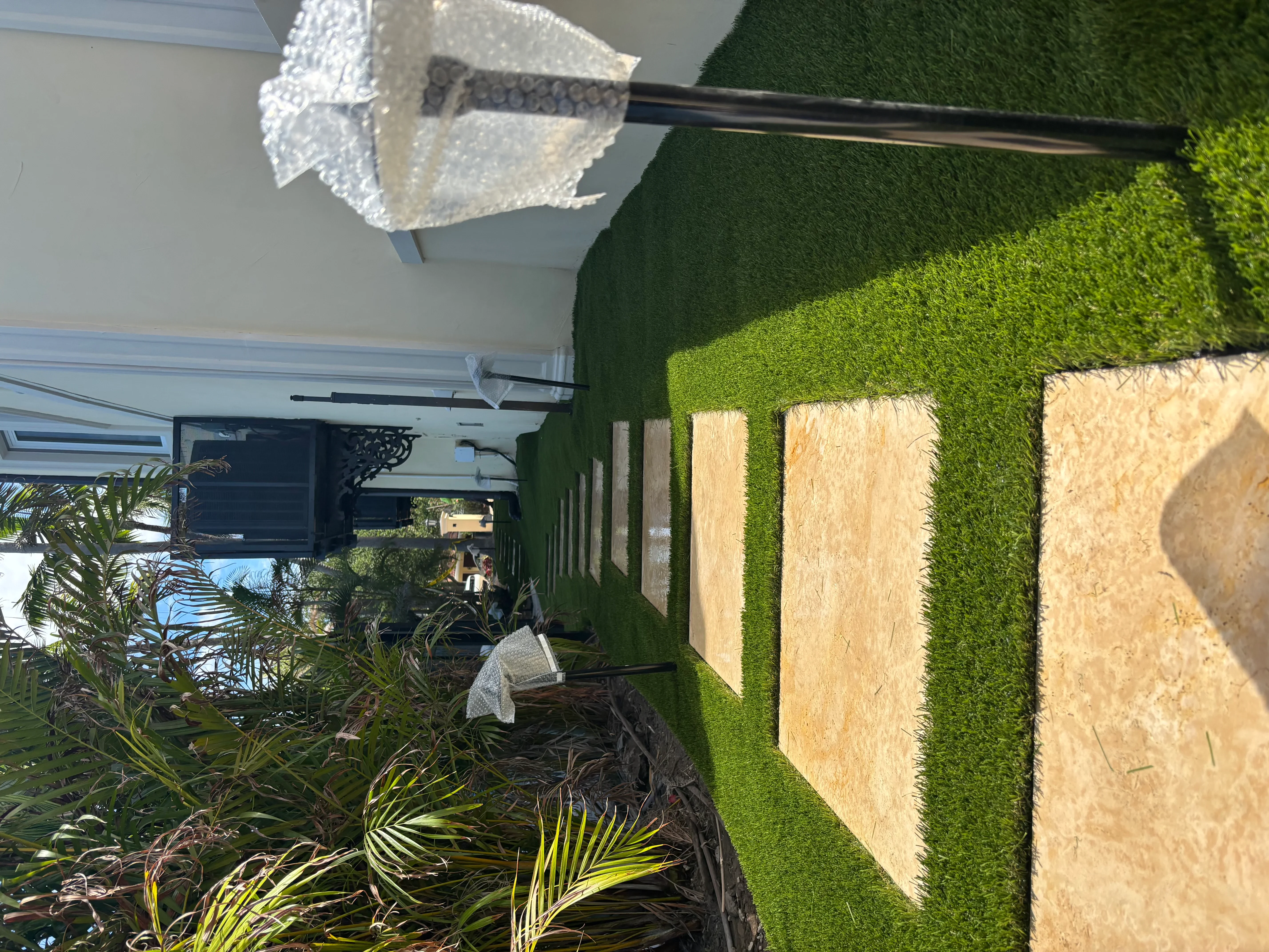 Artificial turf installation with stone planters, tropical plants, and pergola with shade cloth