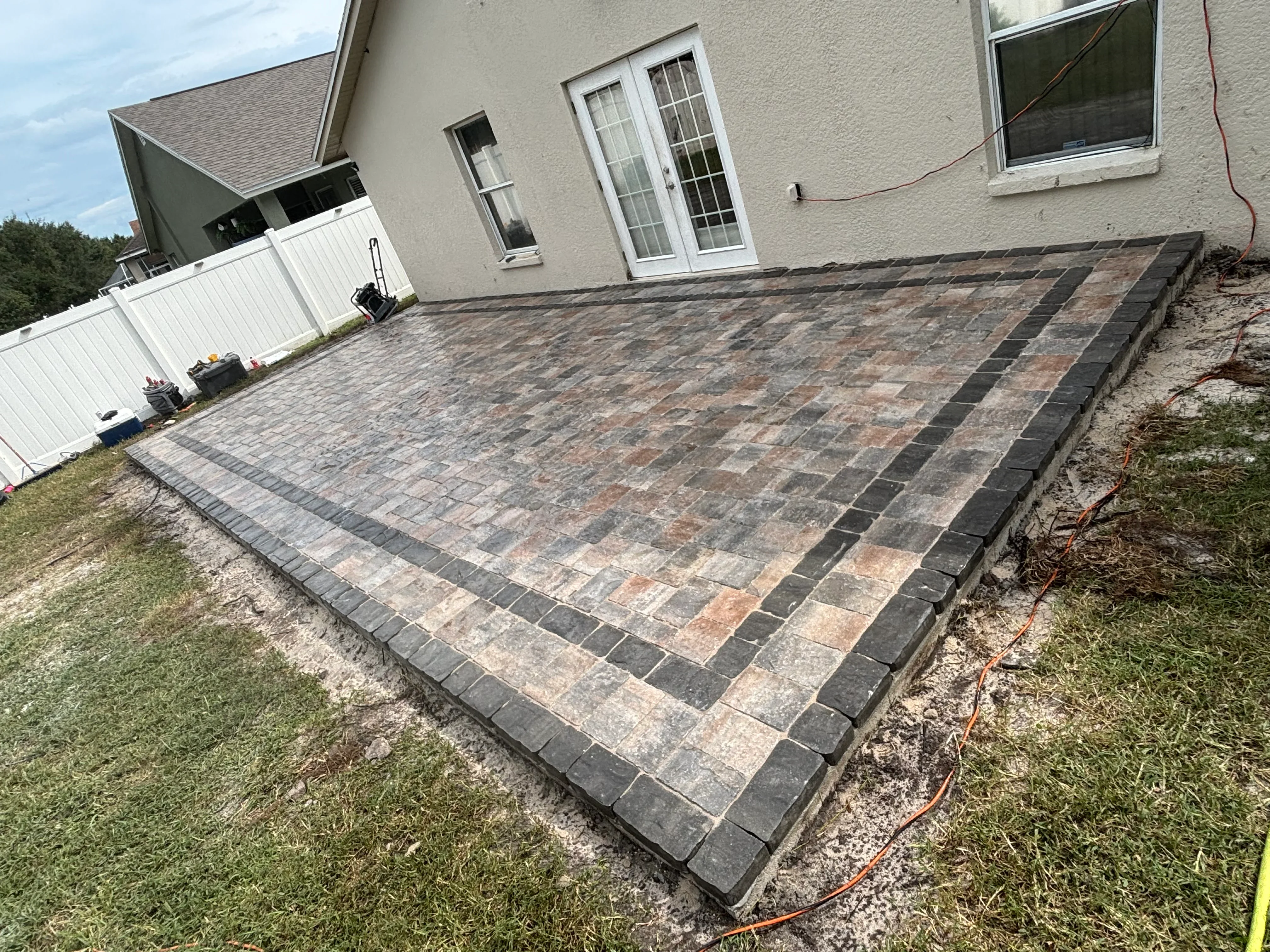 Mixed-tone permeable paver patio with geometric pattern and dark border edging installed at residential home