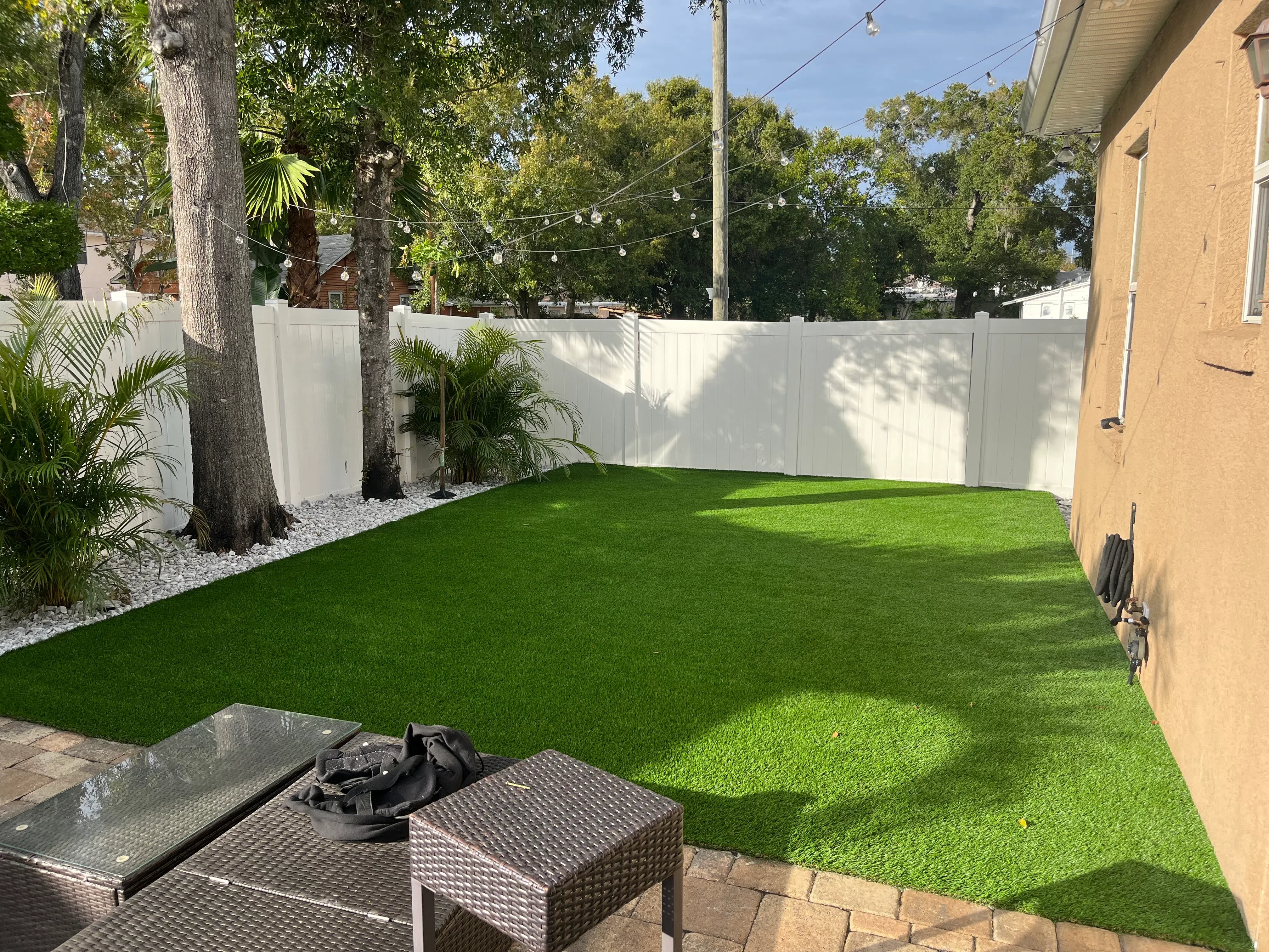 Artificial turf lawn with white vinyl privacy fence, palm plantings, and river rock landscaping