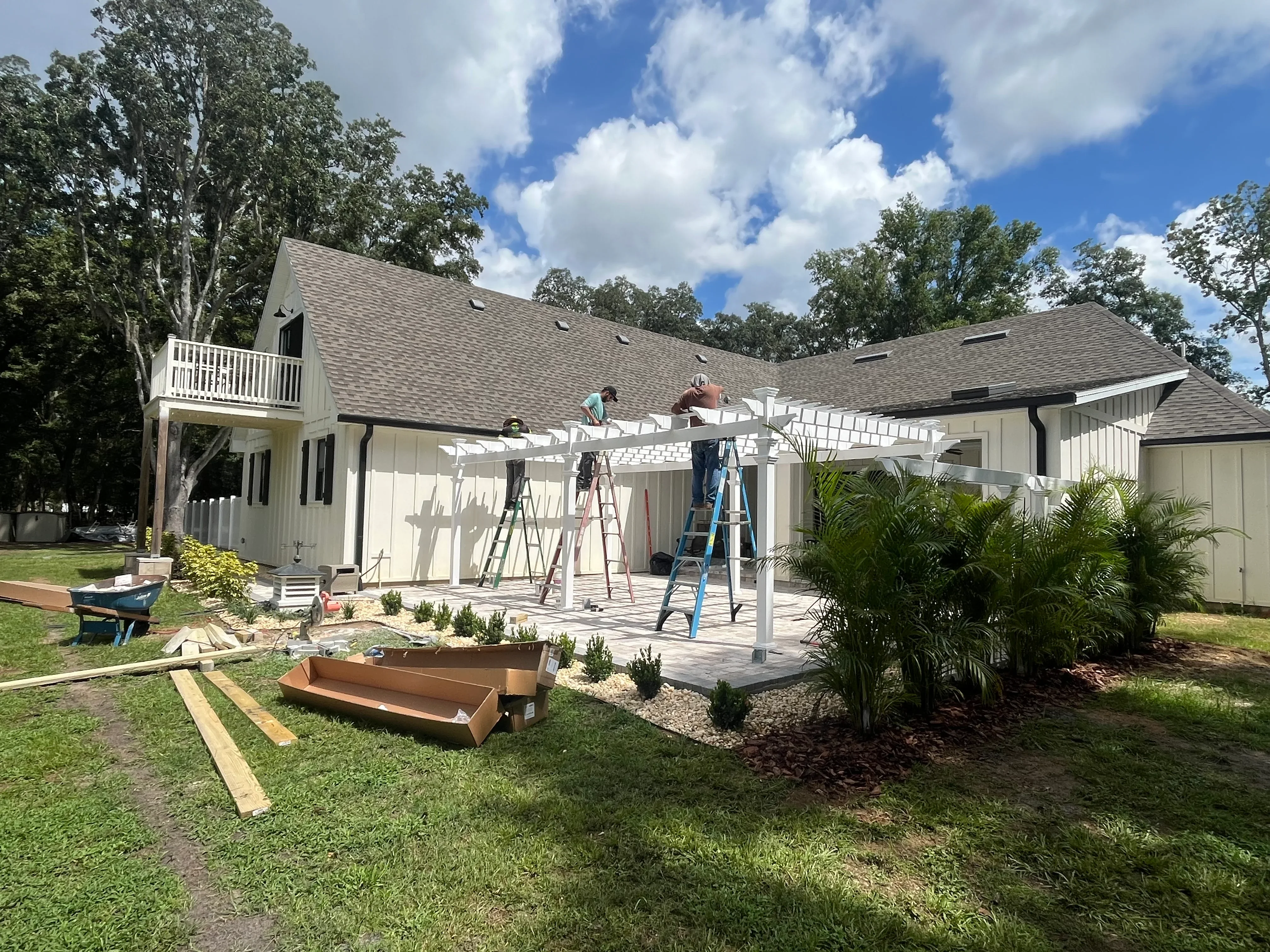 White pergola over composite deck with raised garden beds, palm trees, and mulch landscaping