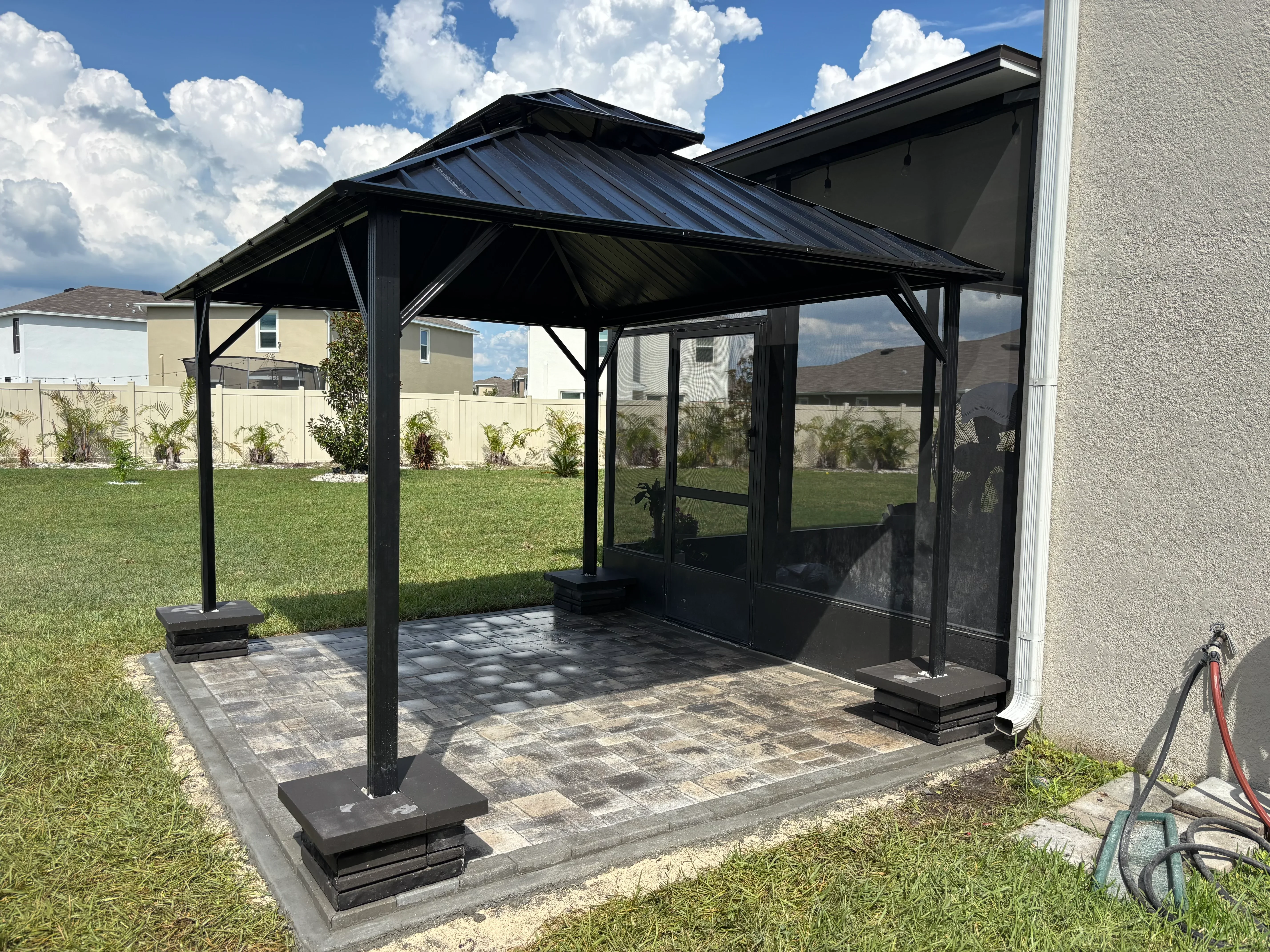 Black metal gazebo with metal roof and screens on paver patio in residential backyard