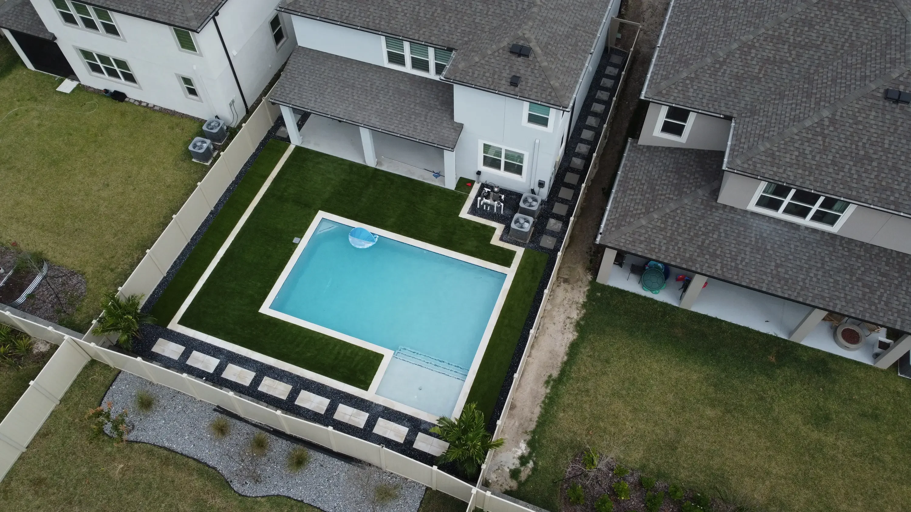 Aerial view of rectangular pool with white coping, synthetic turf surround, concrete deck, and gravel planting beds
