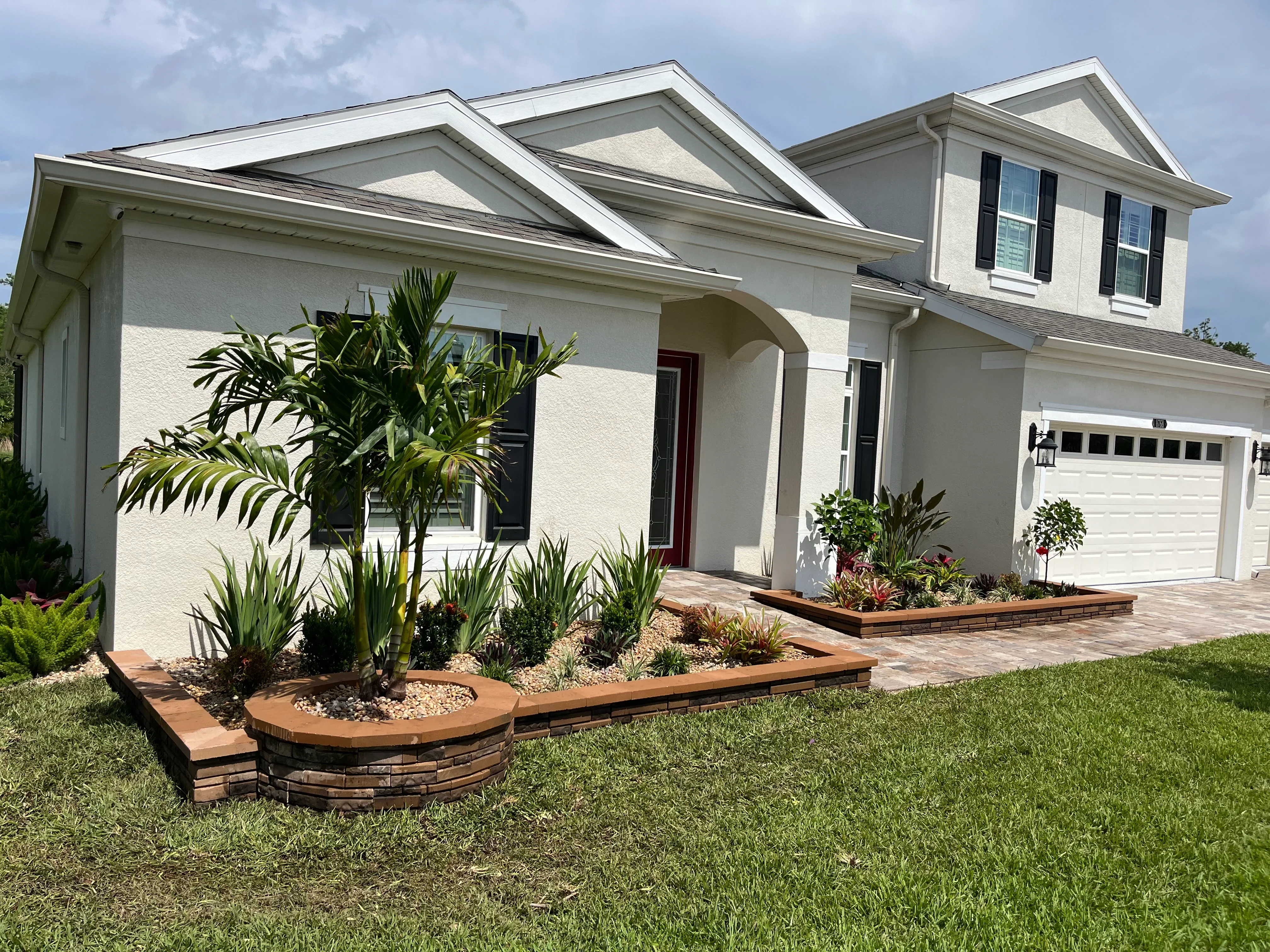 Curved stone and timber planter beds with tropical plants and river rock mulch along home foundation