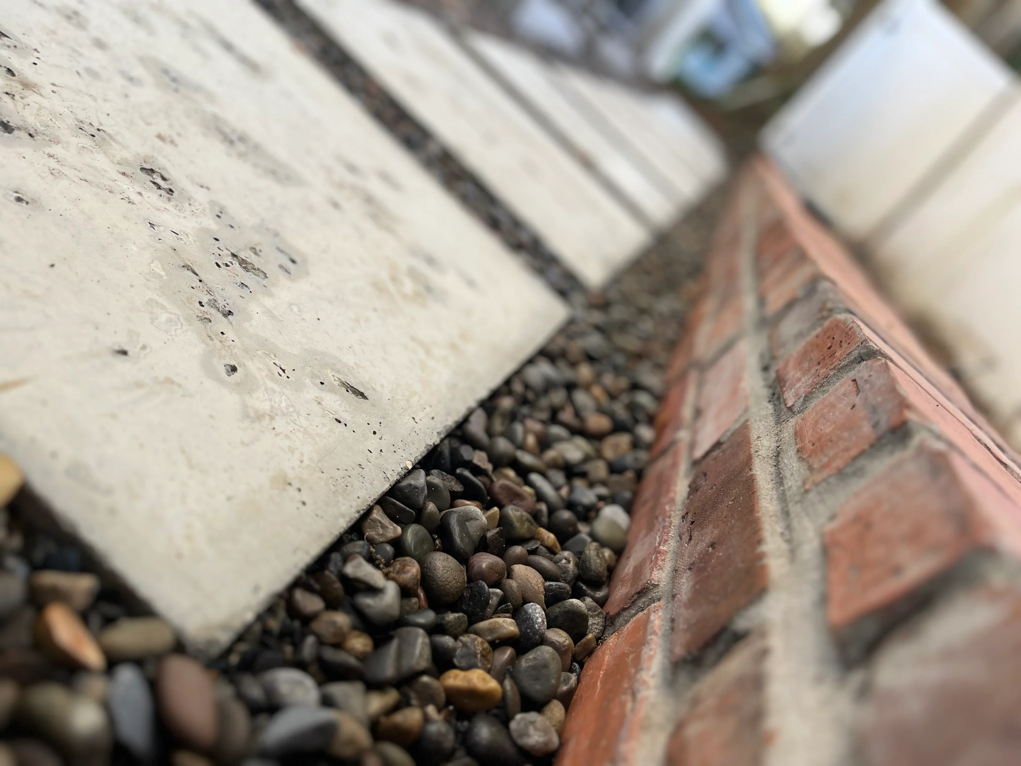 Concrete pavers with river rock and gravel edging along brick foundation