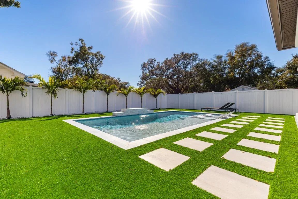 Pool area with synthetic turf, concrete pavers, white vinyl fence, and palm trees