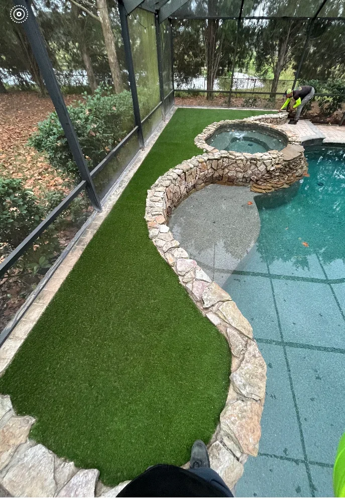 Synthetic turf lawn with curved stone border adjacent to pool and spa with stone surround