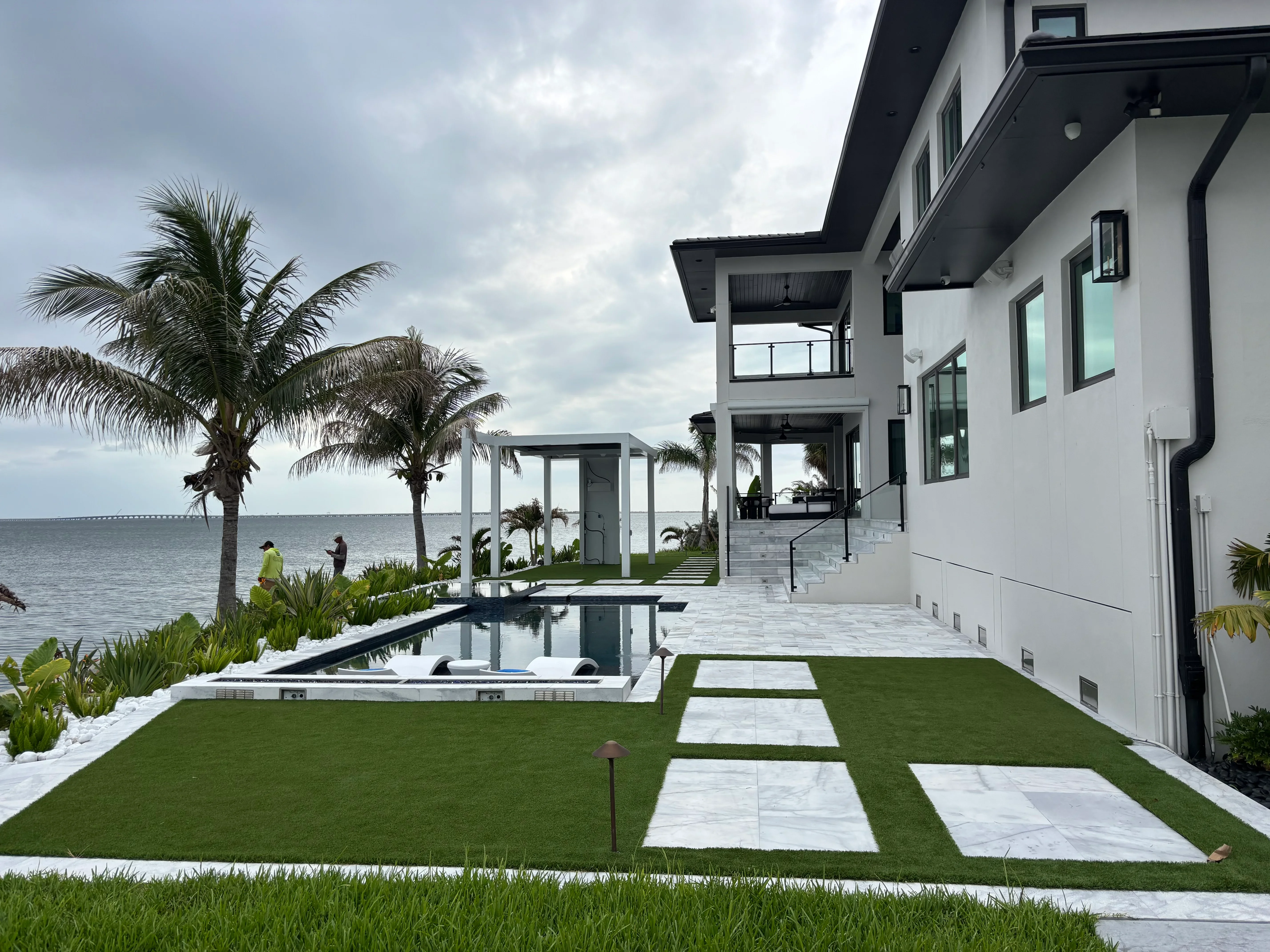 Waterfront home with synthetic turf, stone pavers, tropical palms, and modern hardscape design