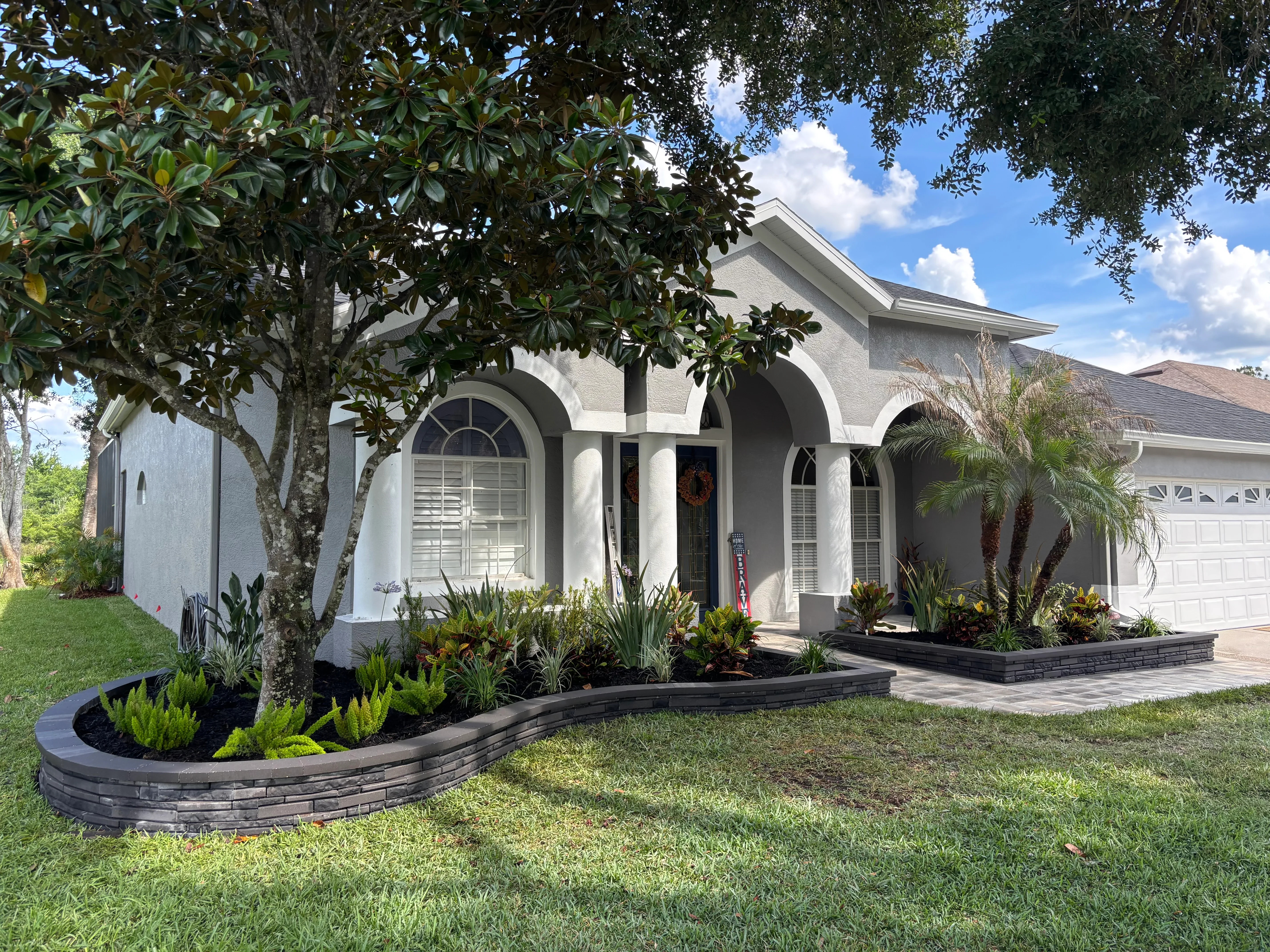 Curved black landscape edging with tropical plants, palms, and mulch beds along home entrance
