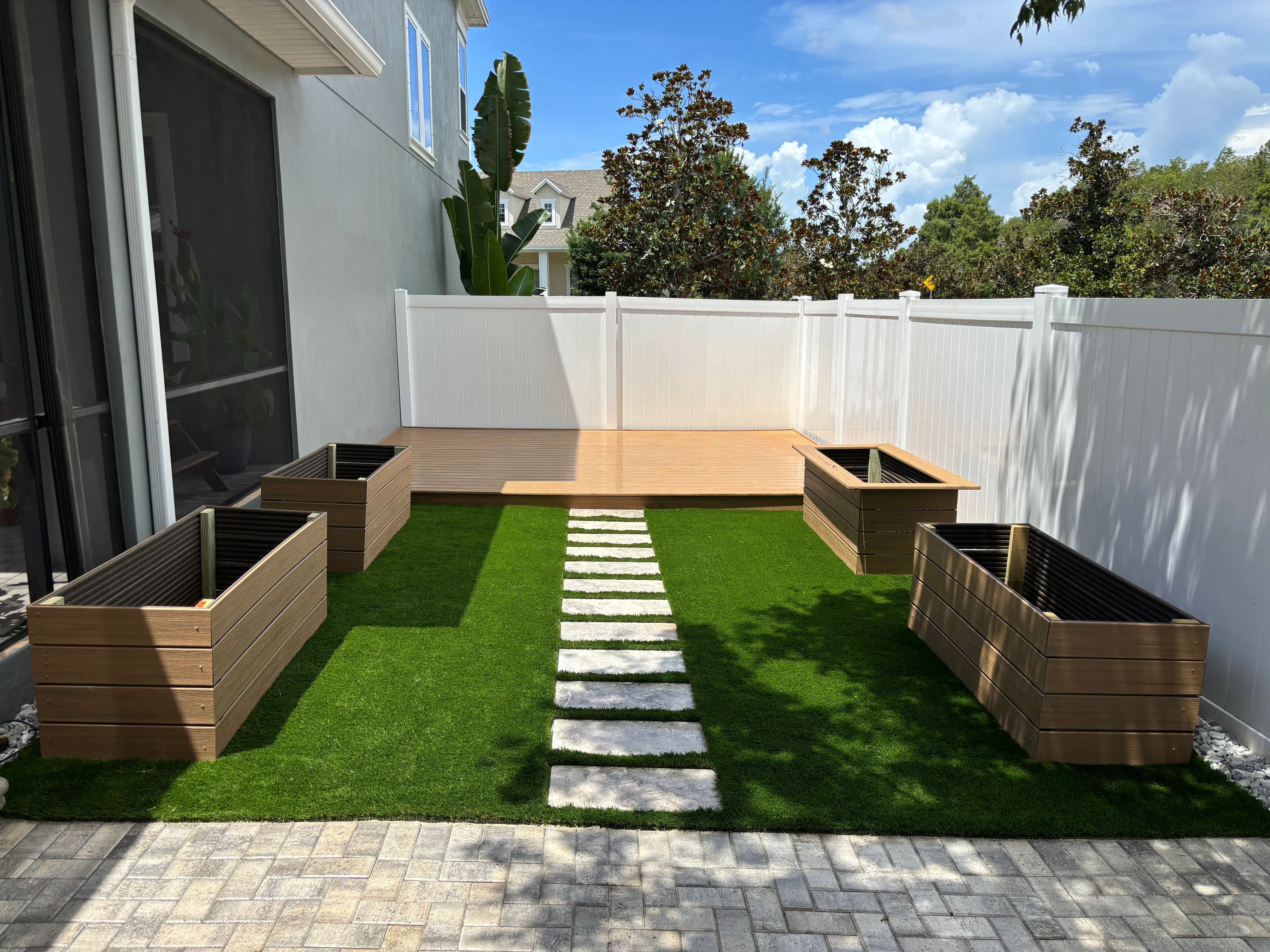 Composite deck with raised wood planters, artificial turf, stepping stones, and white vinyl fence