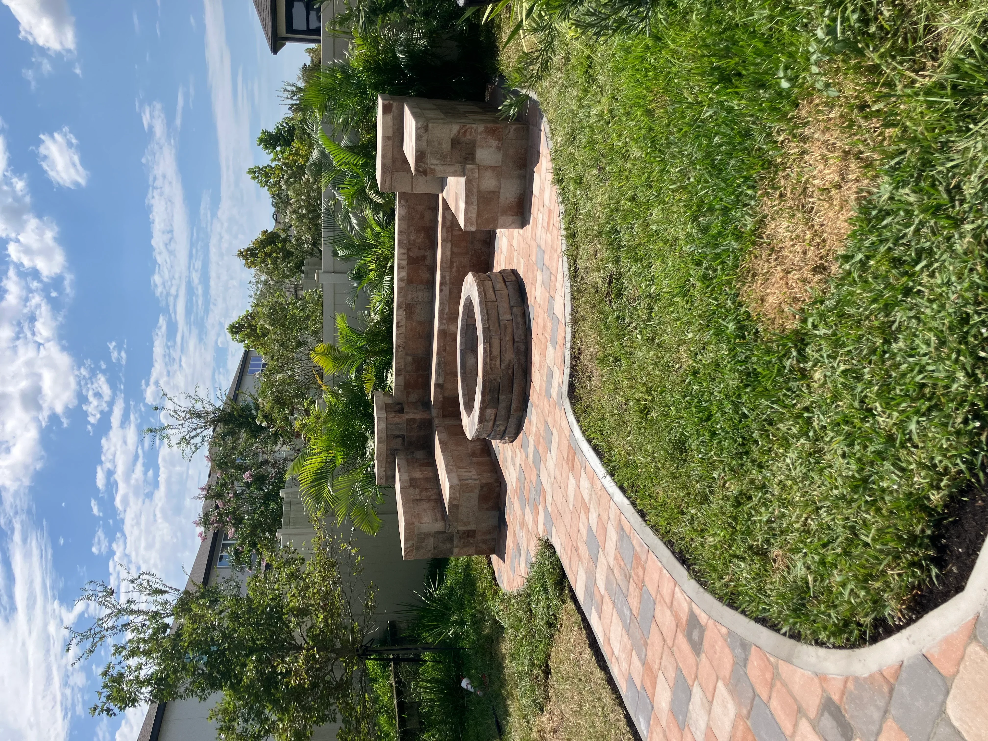 Curved brick planter with dark brick construction and concrete edging surrounded by green shrubs and lawn