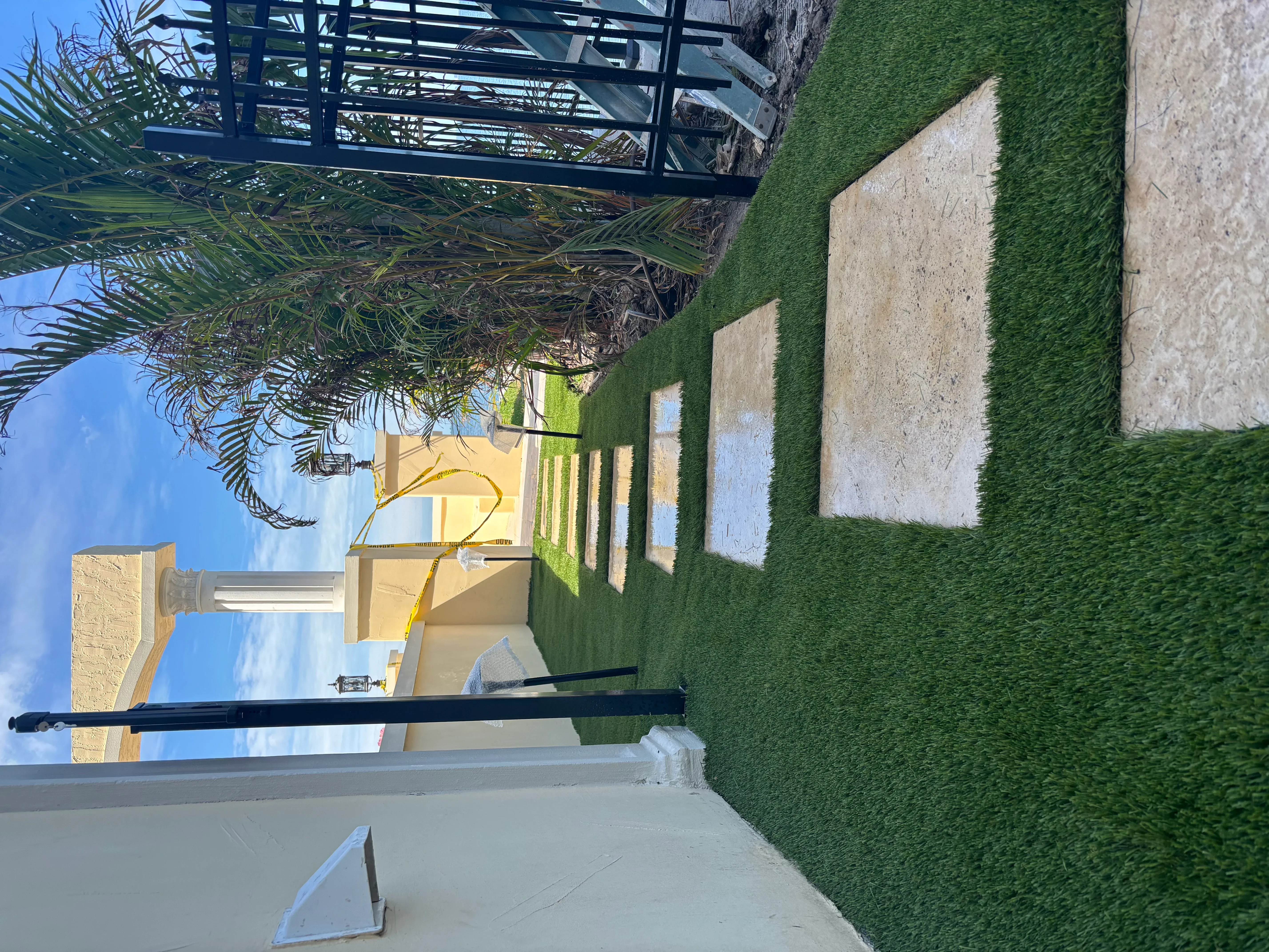 Artificial turf yard with concrete patio, palm tree, and stone wall edging