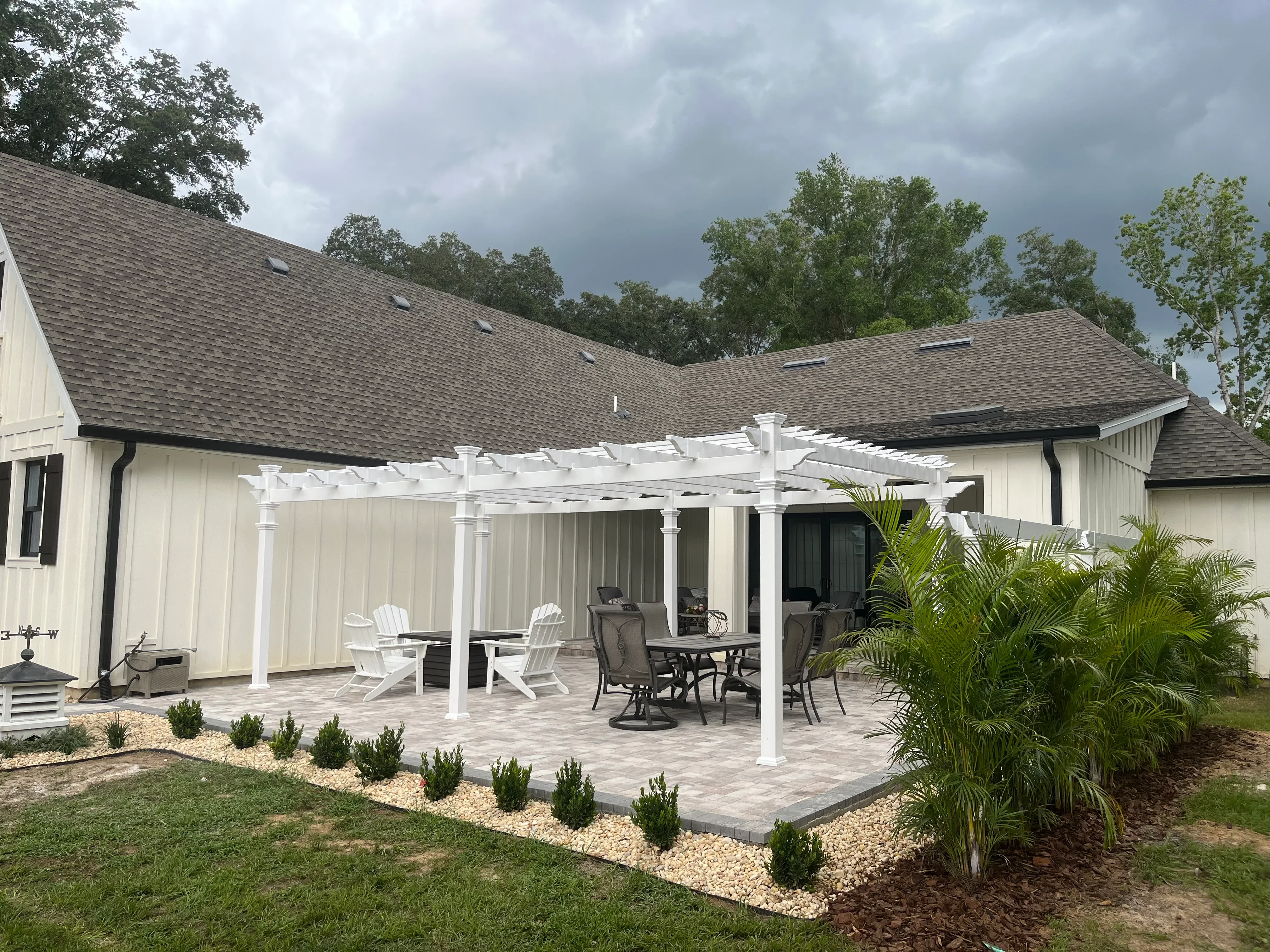 White pergola over paver patio with shrub borders and palm plantings